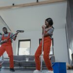 Two adults in vibrant coveralls cleaning a modern home interior, enjoying work.