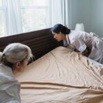 Hotel maids changing bed linens, showcasing professional housekeeping in a bright room.